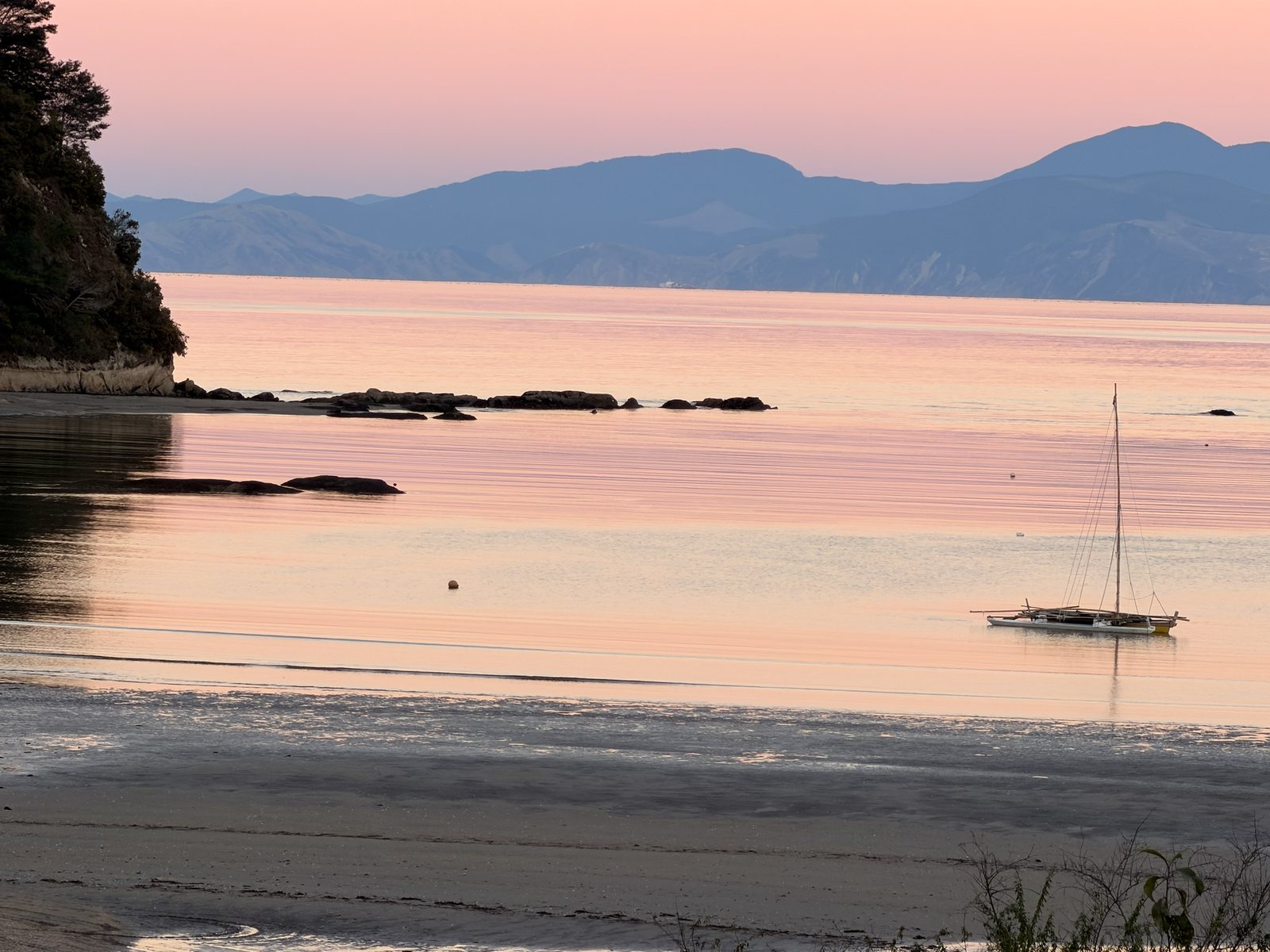 Soft early light over Kaiteriteri bay with a sailboat