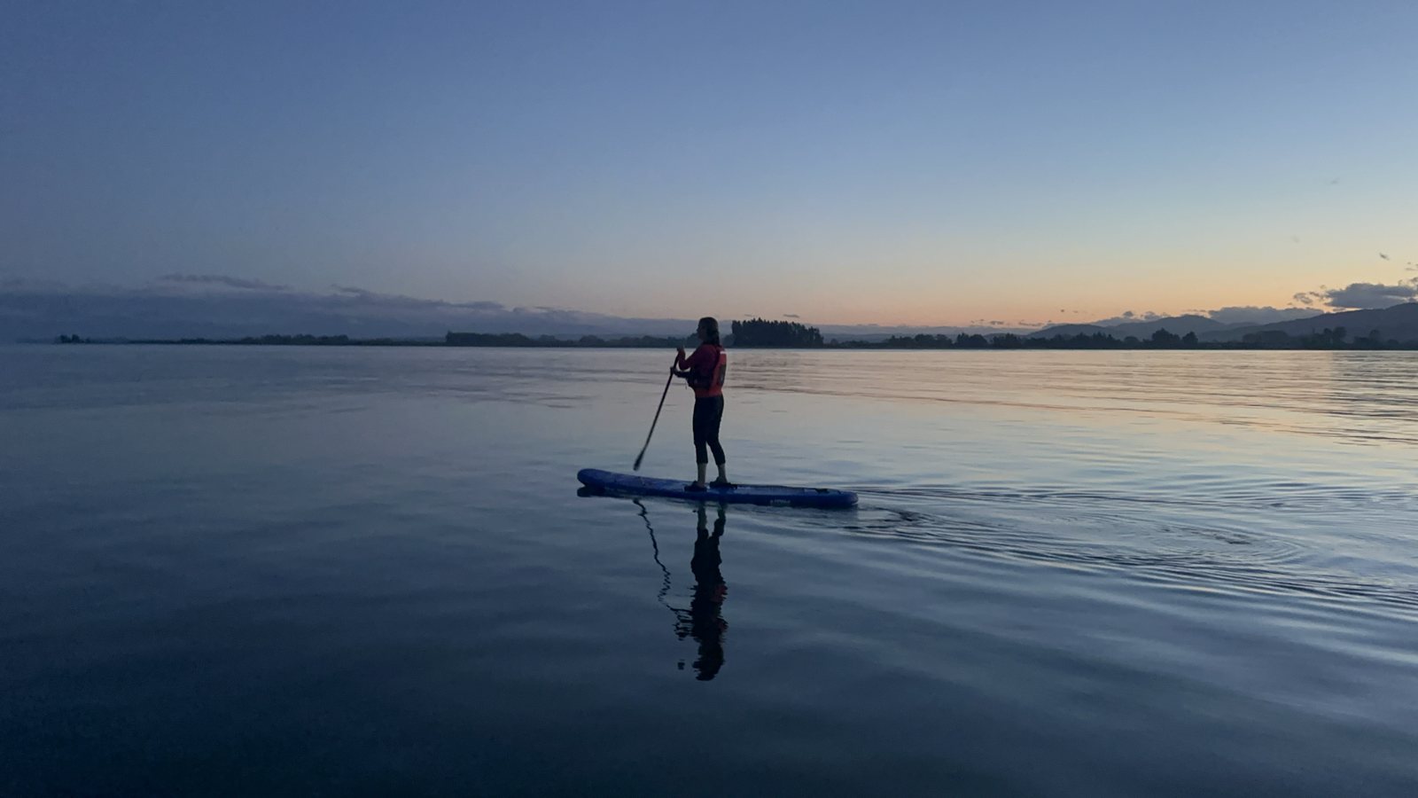Person paddle boarding on calm water at dawn